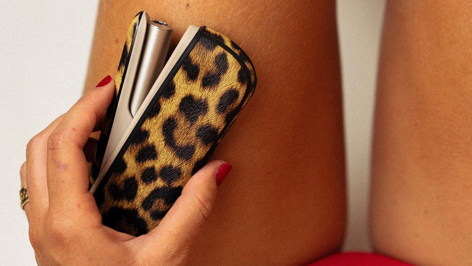 Hand holding a leopard print case against a neutral background
